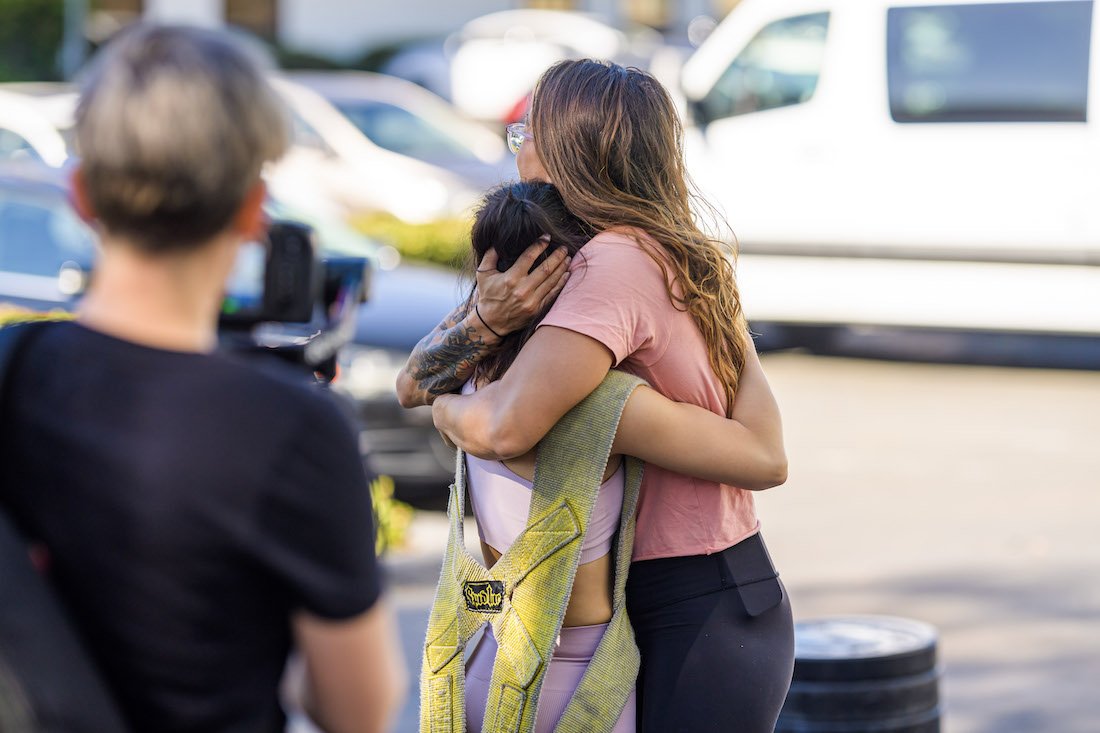 An attendee is embraced with a hug of celebration after overcoming and completing a crossfit workout, pulling a weighted sled with only one arm.