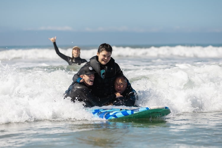 Quad amputee Mia surfs a wave with the help of her two instructors.
