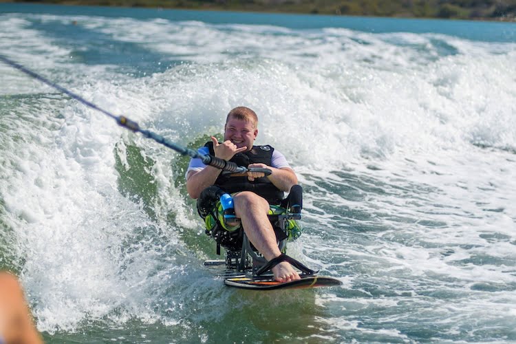 Forge attendee Ethan, a leg amputee, smiles and gives a shaka while wakesurfing on the Carlsbad lagoon.