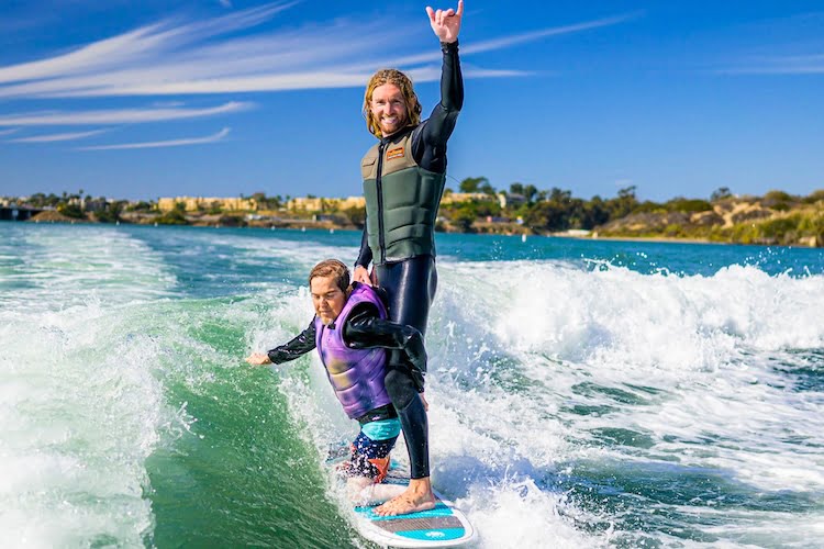Forge attendee and amputee Brett wakesurfs with the help of a leader on the board with him.