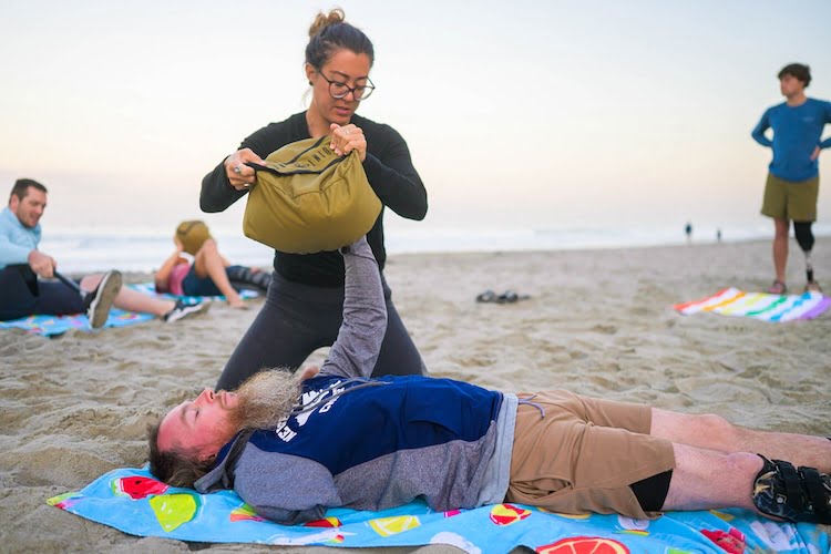 Forge attendee and arm amputee Shane attempts the challenge of lifting a sandbag with his one arm while laying on the beach.