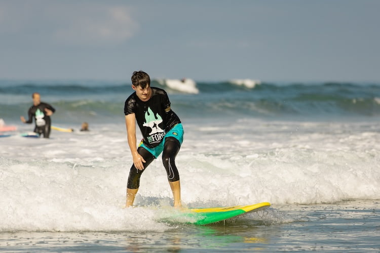 Forge attendee and arm amputee James stands up on his surfboard and rides the wave to shore.
