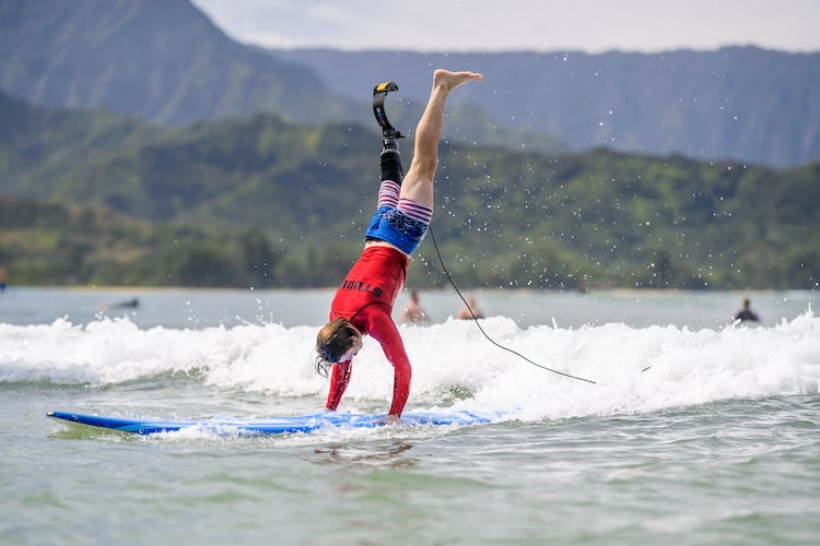 Forge attendee and leg amputee Tyler does a handstand on his surfboard while catching a wave.