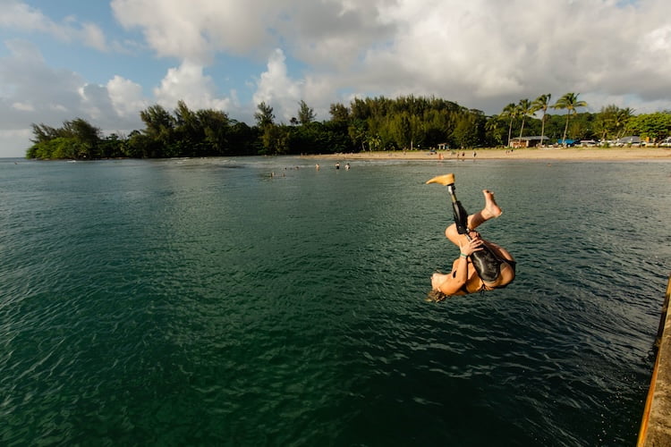 Young women amputee does a backflip off of the Hanalei Pier and into the ocean.