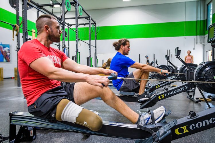 Two Forge men and leg amputees learn to adapt and row on the rowing machine in the CrossFit gym.