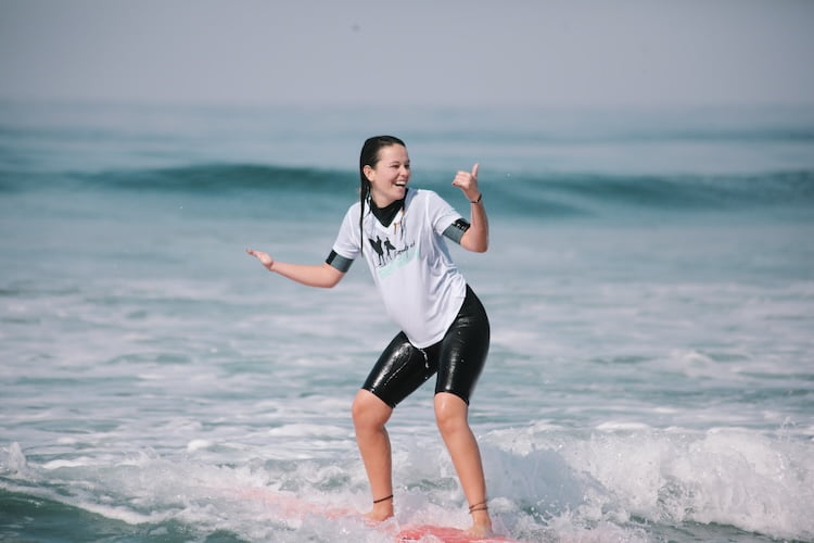 Beautifully Flawed attendee smiles and gives a shaka after adaptively catching a wave and riding it to shore.