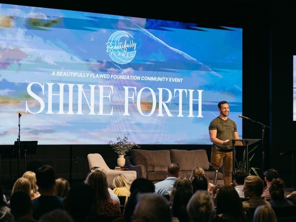 A speaker with a prosthetic leg addresses a seated audience at the Shine Forth event hosted by the Beautifully Flawed Foundation.